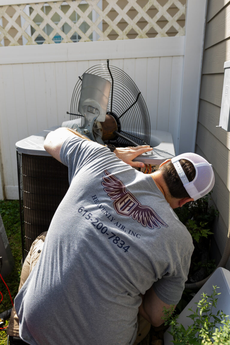 Technician repairing an AC unit beside a home